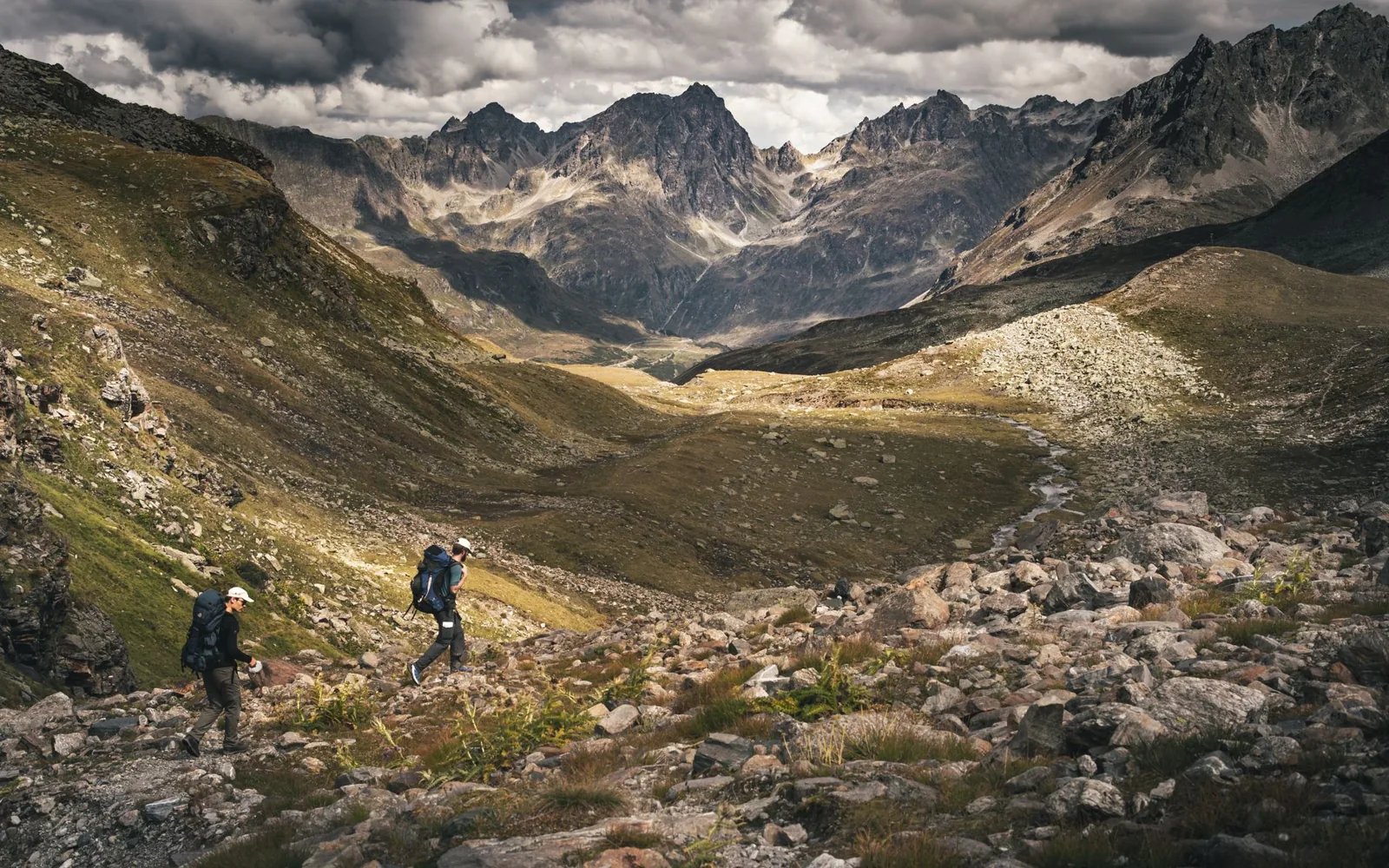 Backpacker with a top-loading pack and trekking poles crossing a mountain pass at dusk